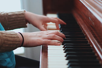 Close-up of hands playing piano keys in cozy sweater