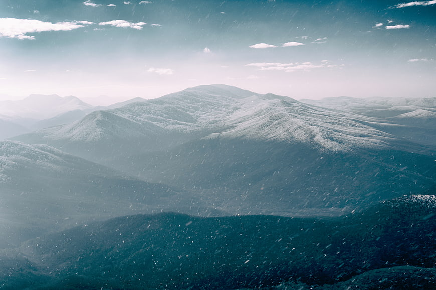 Snowy Mountain Landscape with Falling Snow and Blue Sky