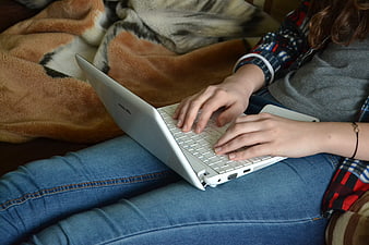 Woman typing on white laptop while relaxing on couch