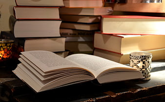 Open book on rustic wooden table with stacked books and candlelight