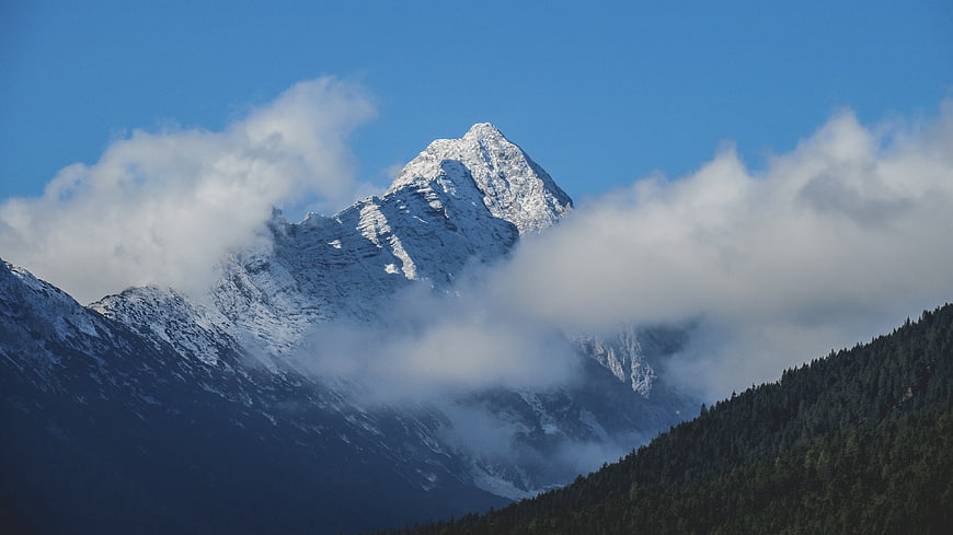 Snowy mountain peak rising above clouds and forest