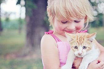 Young girl in pink dress holding an orange and white kitten outdoors