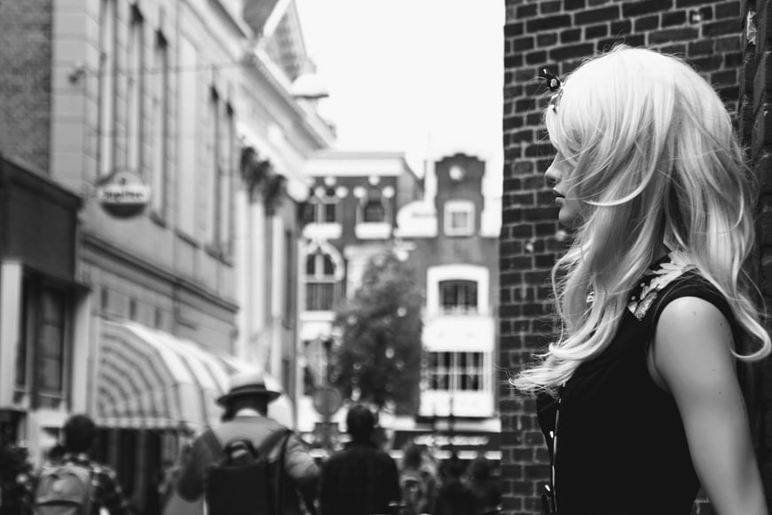 Blonde woman in profile against brick wall on busy street