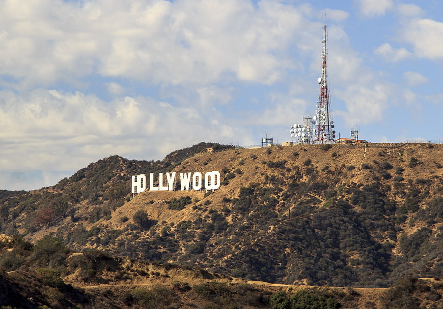 Hollywood Sign on Grassy Hillside with Communication Tower and Cloudy Sky