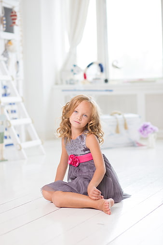 Young girl in a grey dress sitting on a white wooden floor