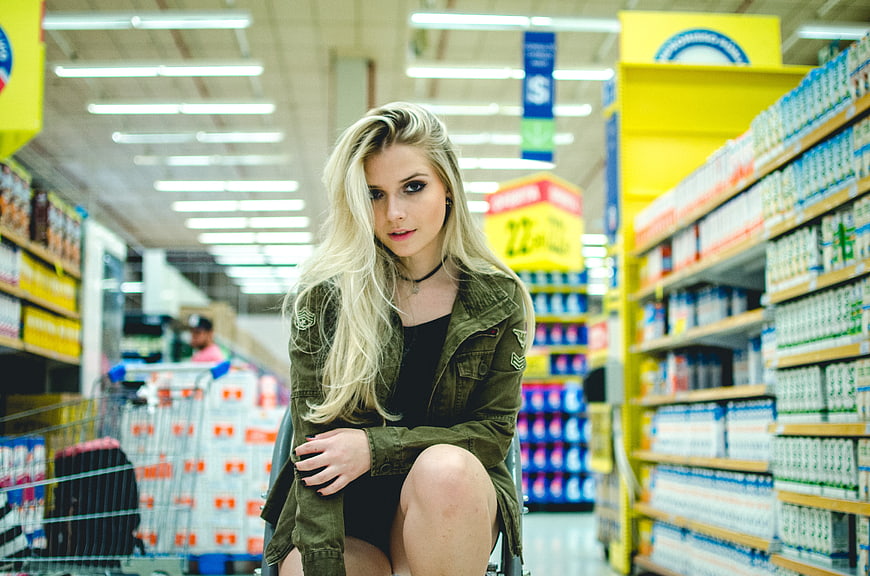 Blonde Woman Sitting in Shopping Cart in Supermarket Aisle