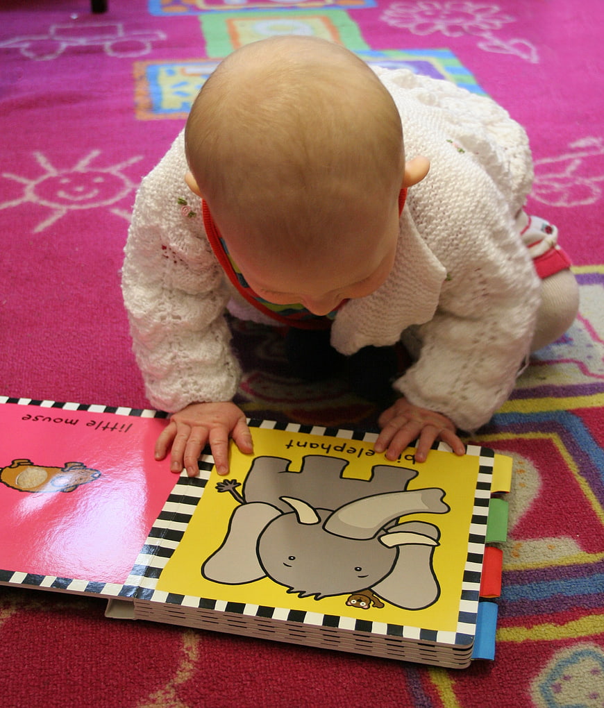 Toddler exploring colorful animal picture book on patterned play mat
