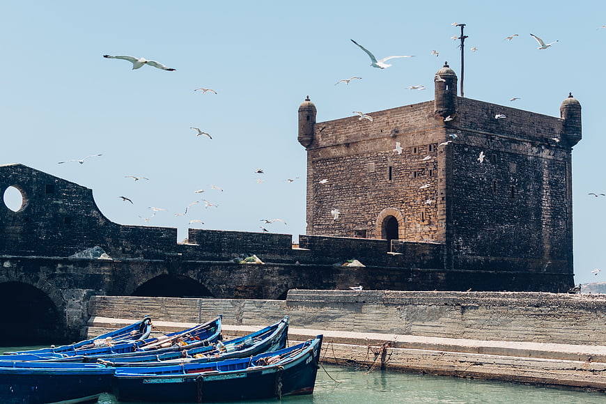 Blue Fishing Boats Docked at Historic Stone Fortress with Seagulls