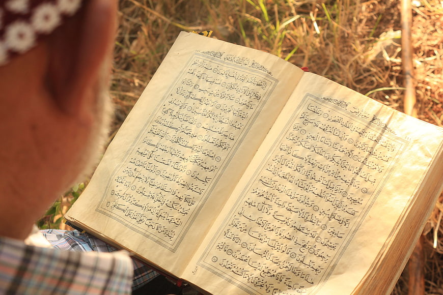 Senior man reading open Quran book outdoors in natural light