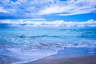 Vibrant Blue Ocean Waves Crashing on Sandy Beach Under Cloudy Sky