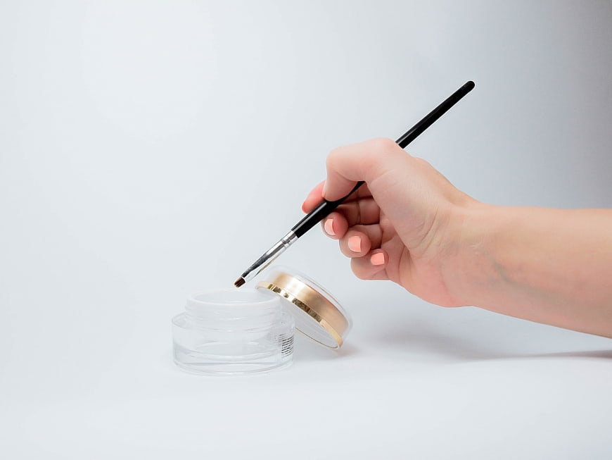 Hand Applying Gel Polish With Brush To Nail Jar