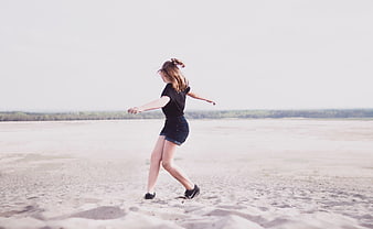 Young woman dancing on sandy beach with arms outstretched