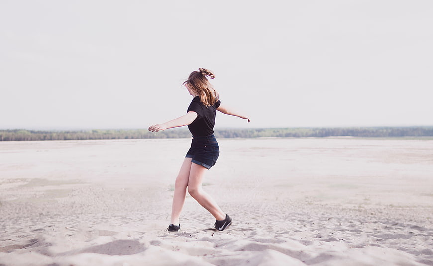 Young woman dancing on sandy beach with arms outstretched
