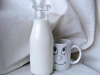 Glass bottle of milk and smiling face mug on white cloth