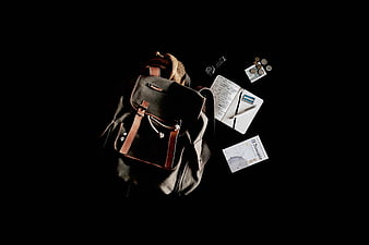 Travel backpack with passport, notebook, and coins on black background
