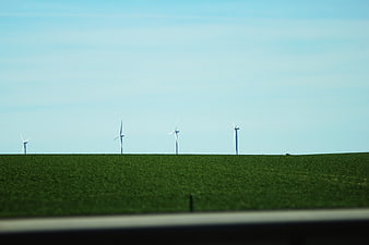 Wind turbines on green hill against blue sky
