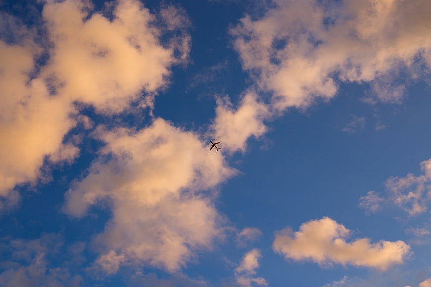 Airplane flying through blue sky with golden clouds