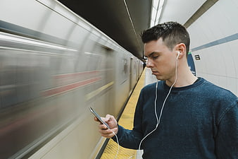Man with Earphones Using Smartphone on Subway Platform