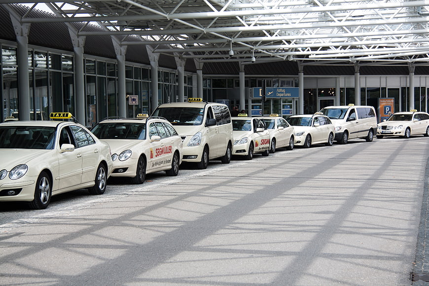 Row of white taxis parked at airport terminal taxi stand