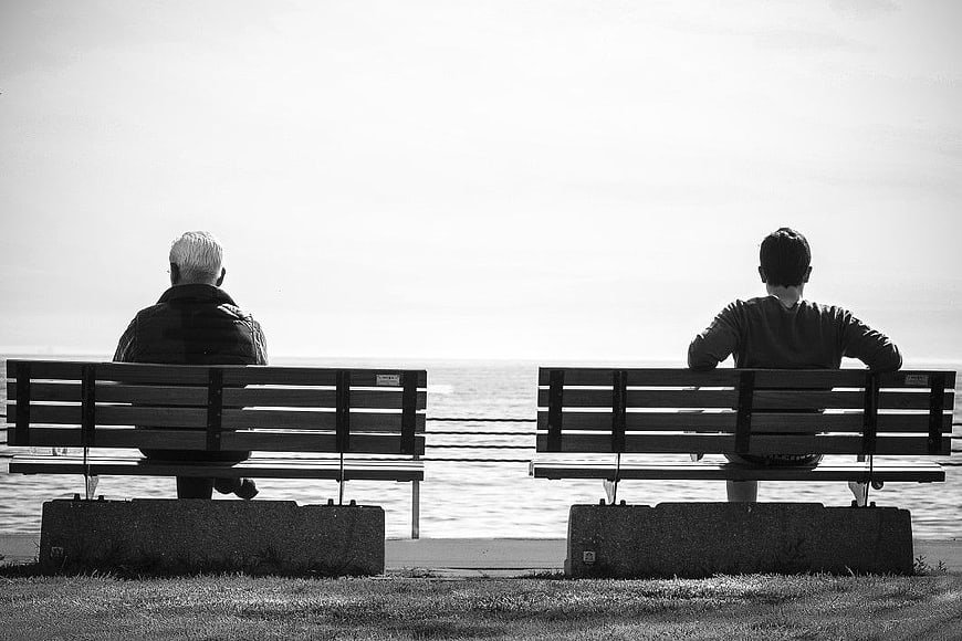 Two Men Sitting on Separate Benches by the Sea