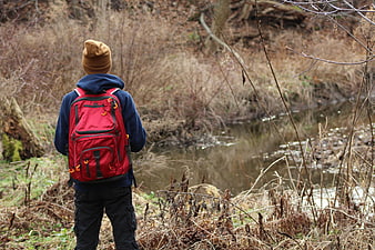Hiker with Red Backpack Standing by Stream in Woods