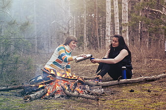 Two women camping and drinking by a bonfire in the forest