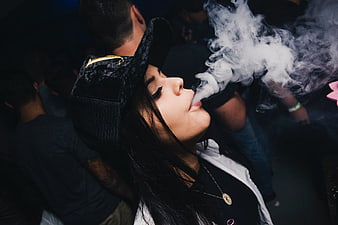 Woman exhaling thick vape smoke in dark club setting