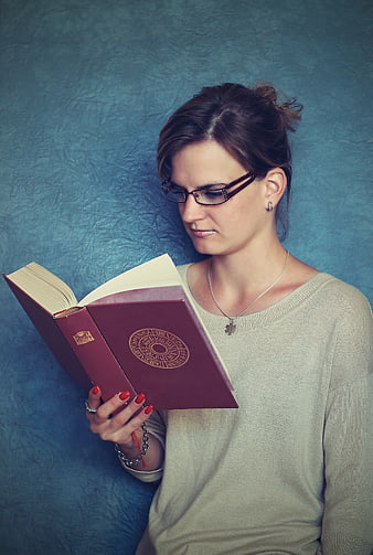 Young woman with glasses reading a red hardcover book against a blue background
