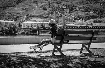 Young woman resting on bench with roller skates by river