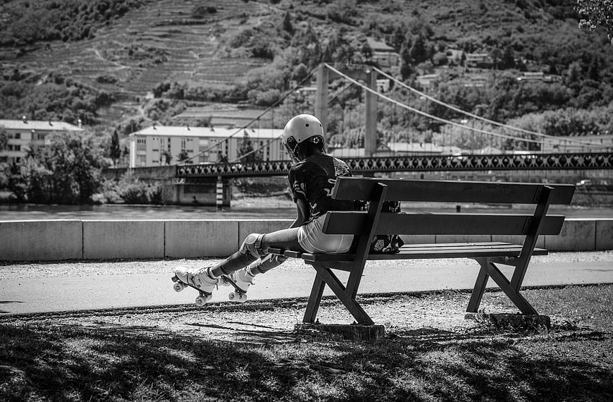 Young woman resting on bench with roller skates by river