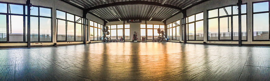 Panoramic view of empty modern gym with wooden floors and large windows