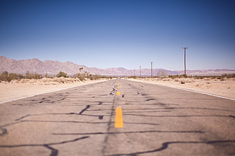 Cracked Desert Highway Leading To Distant Mountains Under Blue Sky