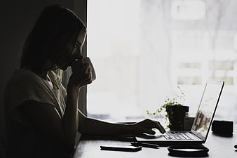 Woman working on laptop with coffee by window
