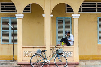 Man resting on yellow building porch with bicycle