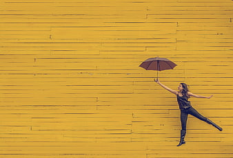 Woman Jumping with Umbrella Against Yellow Wall