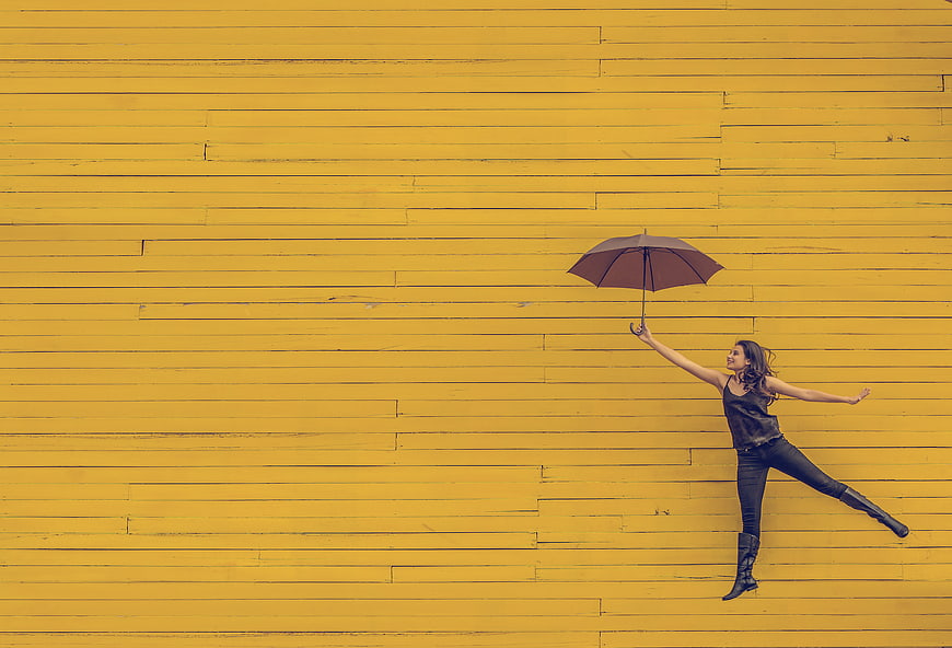 Woman Jumping with Umbrella Against Yellow Wall