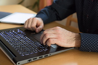 Close-up of male hands typing on a backlit laptop keyboard