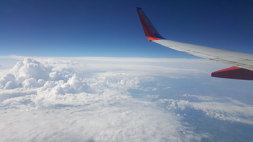Airplane wing over clouds with blue sky