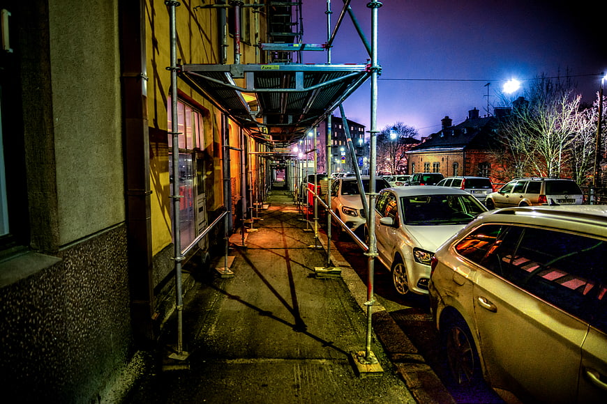Urban street at night with scaffolding and parked cars