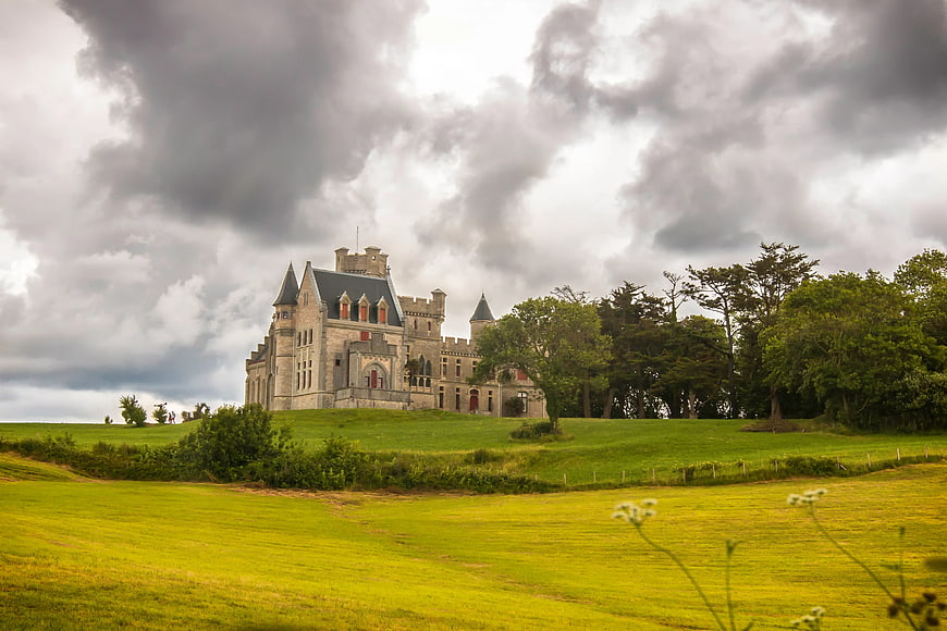 Historic stone castle on green hill under dramatic cloudy sky