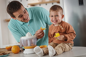 Happy Father and Son Making Fresh Orange Juice in Kitchen