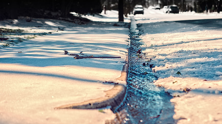 Low angle view of melting snow and water runoff on a winter street curb