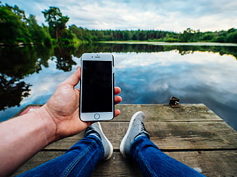 Man holding smartphone on wooden dock by lake