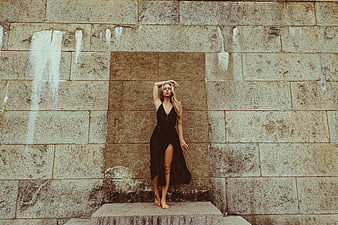 Blonde woman in black dress posing against textured stone wall