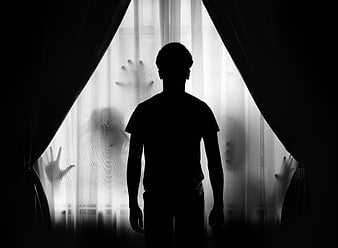 Silhouette of man standing before window with ghostly hands on glass