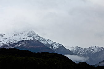 Snow-Capped Mountain Peaks Rising Above Dark Forest