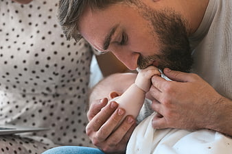 Close-up of bearded father kissing baby's hand