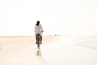 Woman riding bicycle on sandy beach shoreline