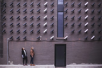 Two women standing under wall of surveillance cameras
