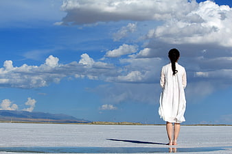 Woman in White Dress Standing on Salt Flat Under Blue Sky